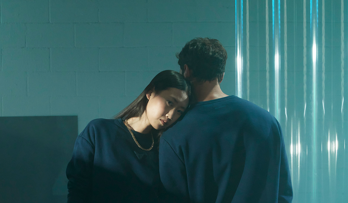 Frau lehnt ihren Kopf auf die Schulter eines Mannes, beide tragen dunkelblaue Sweatshirts aus der CUPRA Collection, im Hintergrund metallisch glänzende Wandstruktur.